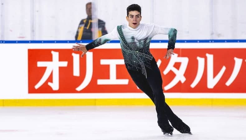 Jacob Sanchez skates forward his arms out to the side. He wears black pants and a white, green and black top.